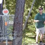 Disc golfer approaching a basket on a wooded course