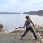 Young disc golfer throwing from a tee pad by a lake