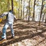 Disc golfer throwing on a wooded course