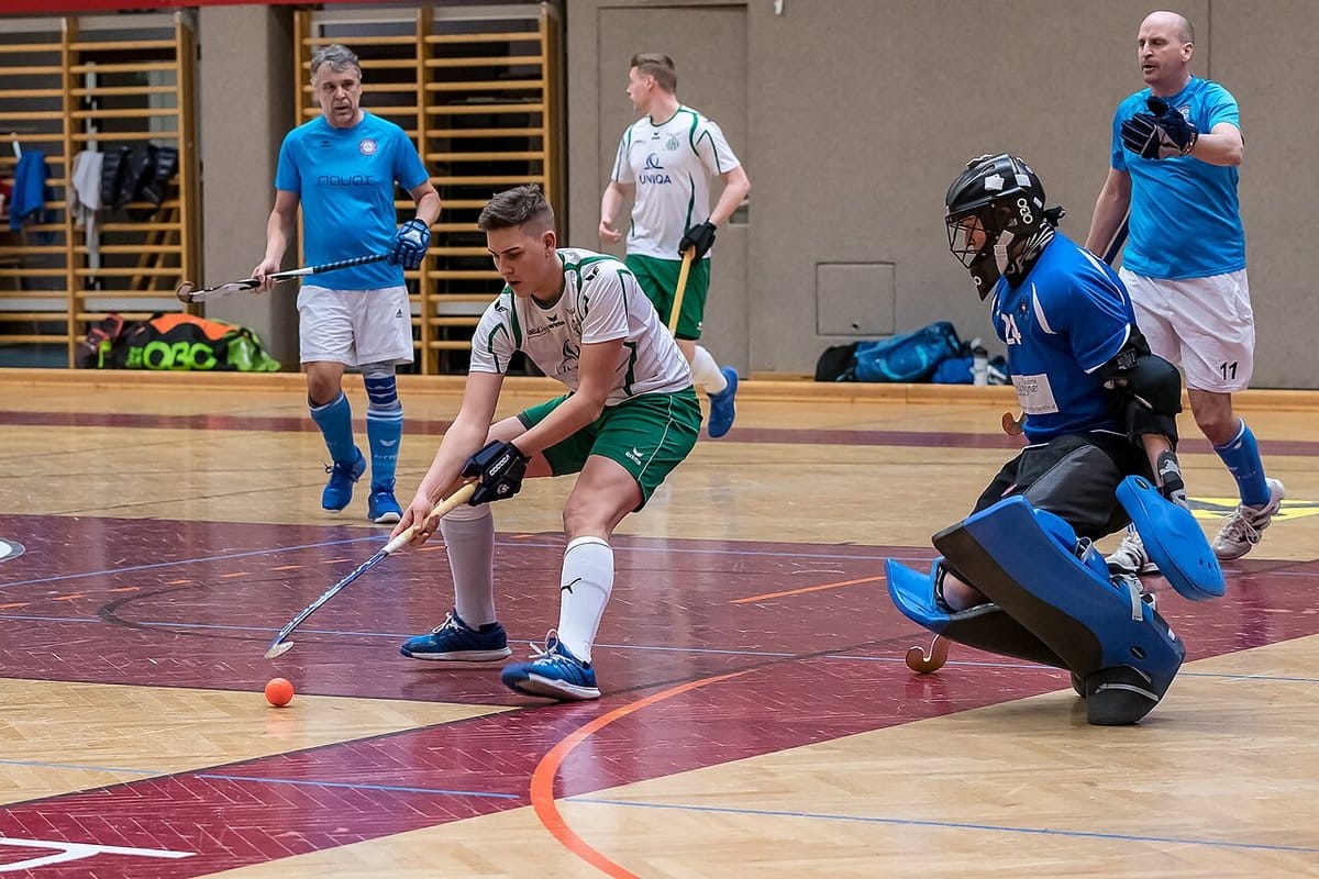 Hockey goalkeeper in full pads blocking a shot indoors