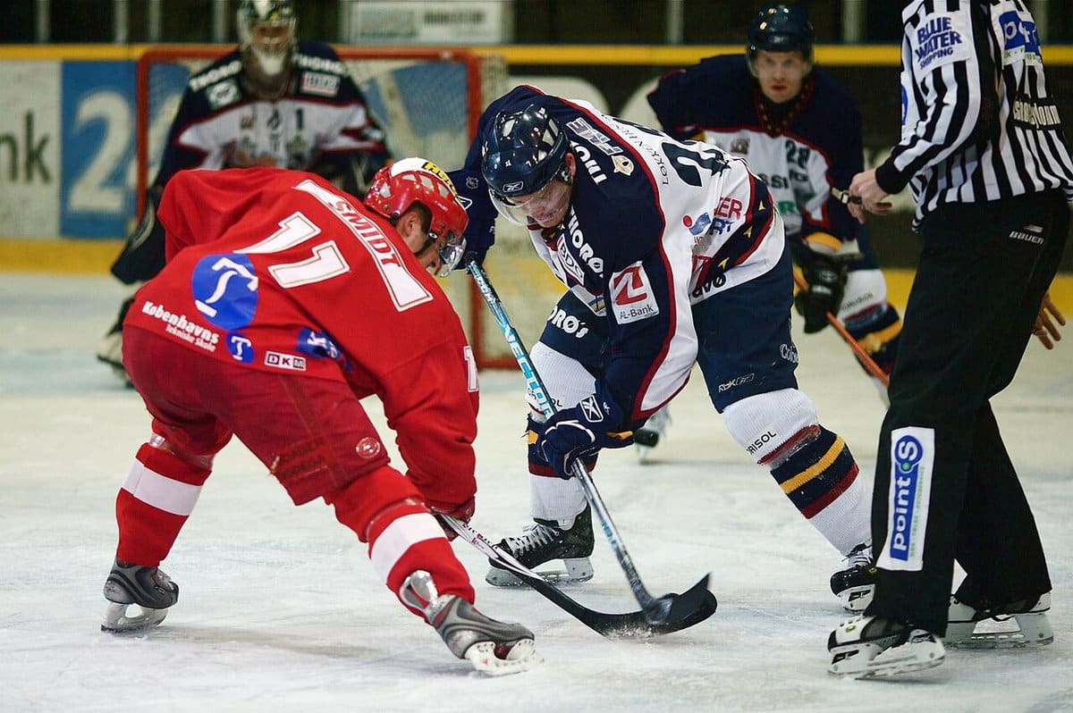 Two centers battling for the puck at a faceoff with the referee