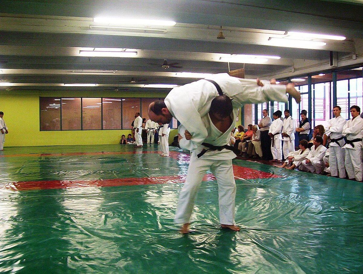 Judo class practicing on green mats in a dojo