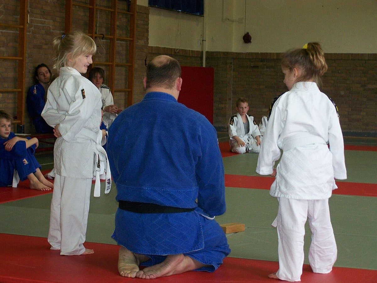 Children in judo gis with their instructor on the mat