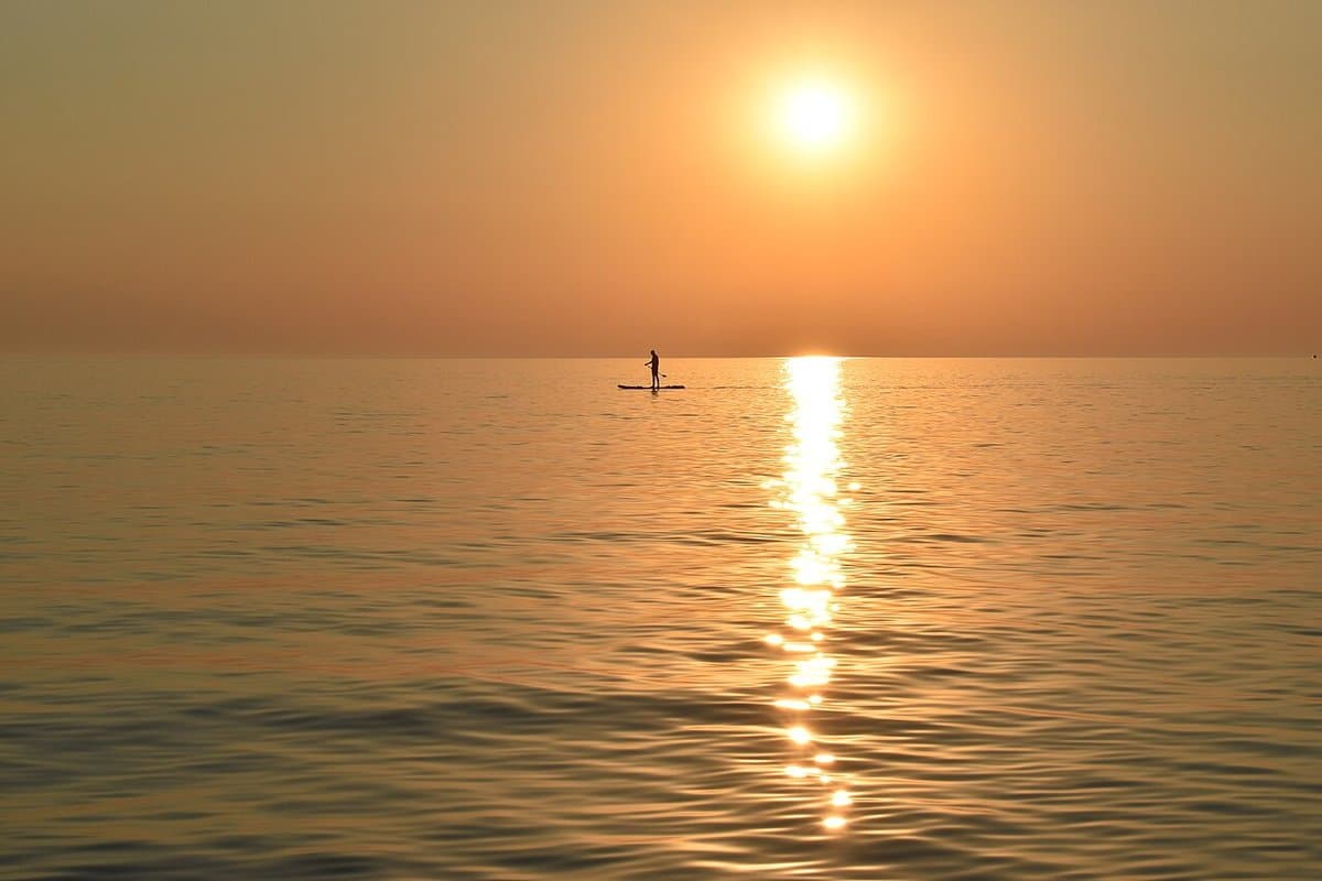 Lone paddleboarder silhouetted against a golden sunset
