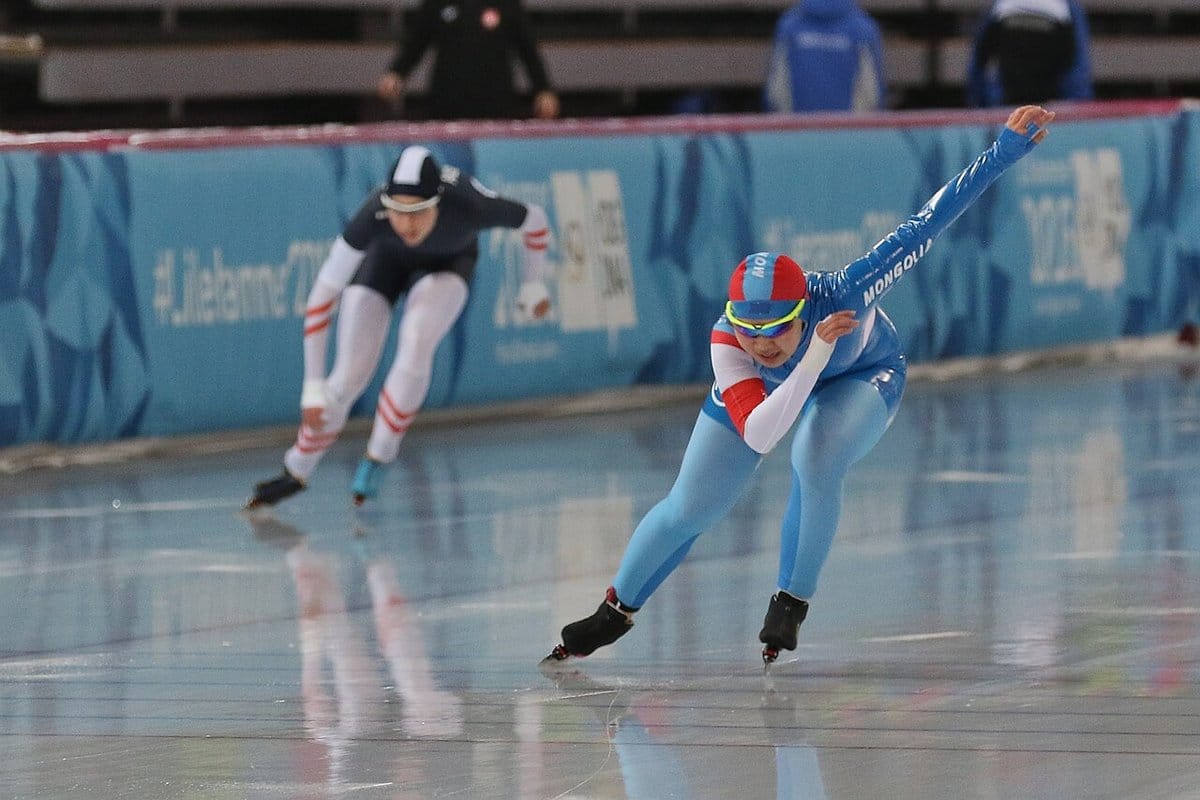 Women speed skaters racing side by side on the oval