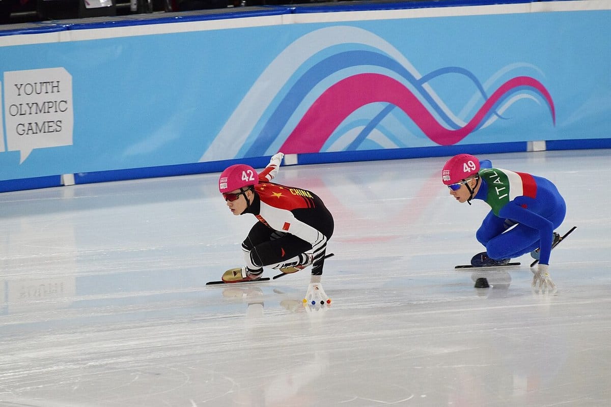 Two short track skaters leaning low through a corner