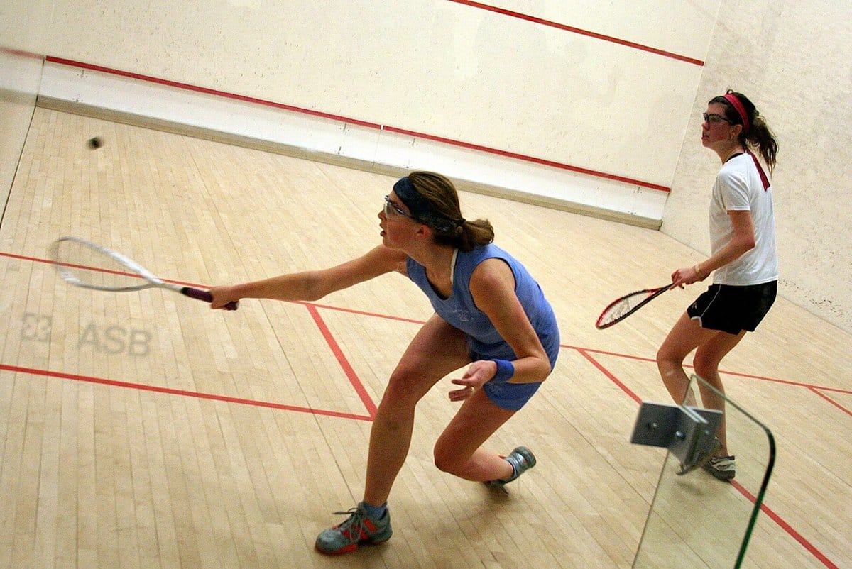 Two women squash players chasing a tough return