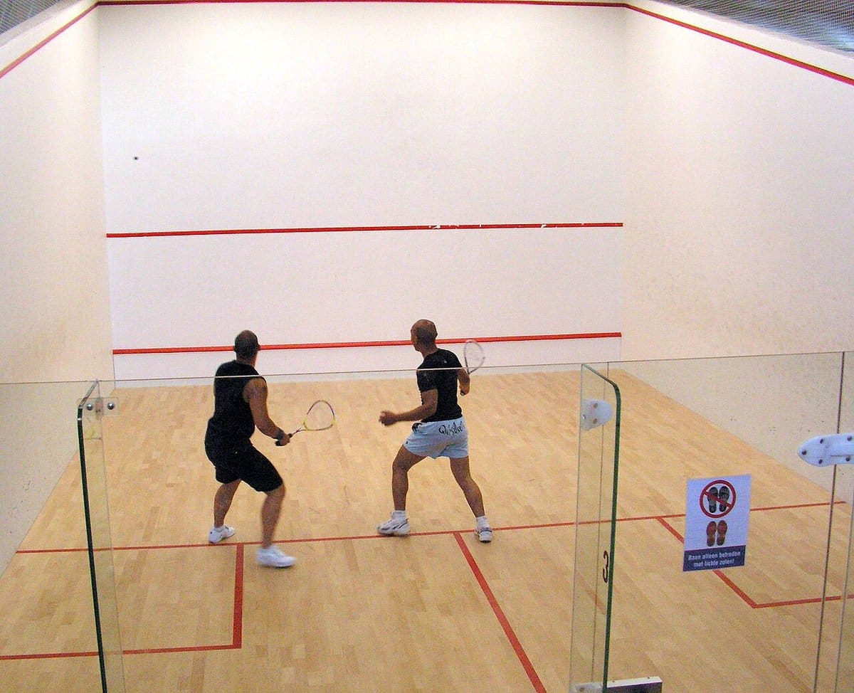 Two players in a rally on a white squash court