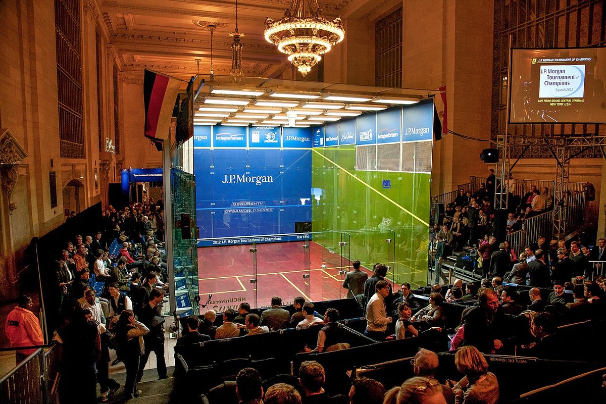 Glass squash court set up for a tournament in front of a full crowd