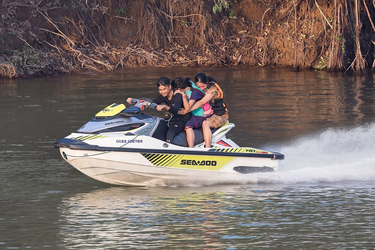 Three friends riding a jet ski across a river